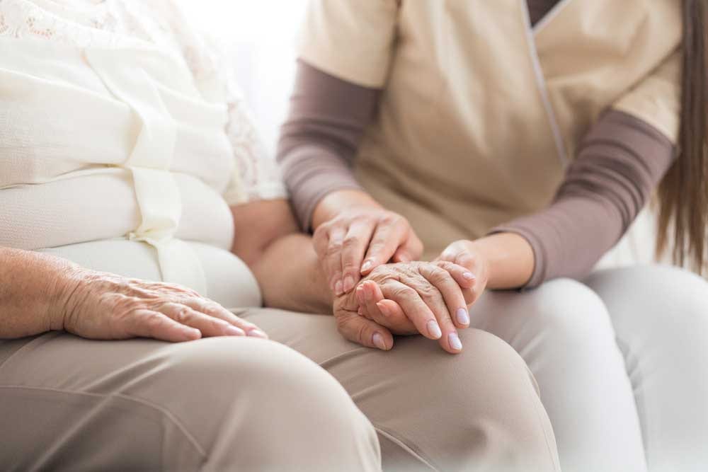 badante che prende la mano tremolante di una malata di Parkinson